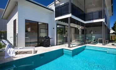A modern pool with daybeds, glass fencing and an overlooking balcony
